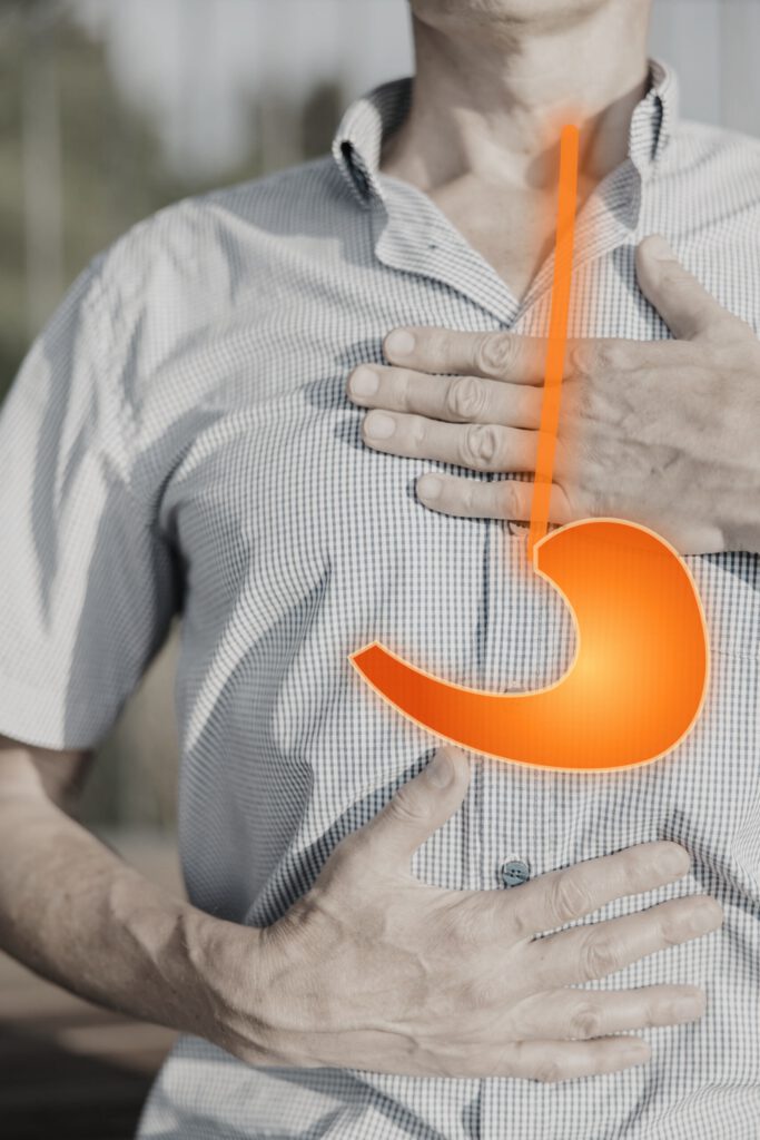 Mann hält sich Brust und Oberbauch, Magen und Speiseröhre leuchten orange – Sodbrennen und Reflux